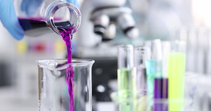 Bright purple liquid flows steadily from a glass container into a clear beaker filled with colorful solutions.