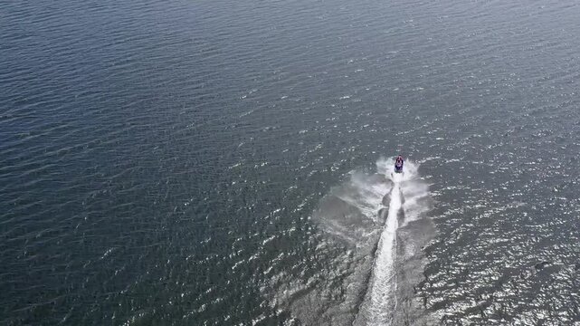 On a bright afternoon, thrill-seekers race across serene waters on their jet skis, creating splashes and joyous laughter. The sun reflects on the waves, adding to the thrill.