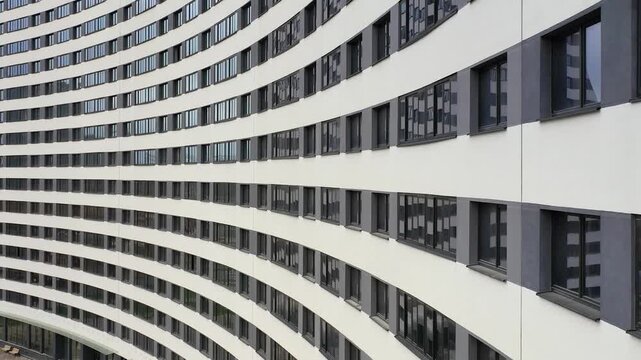 An elegant building showcases flowing lines and curves under bright daylight. Sunlight reflects off the glass, creating stunning patterns. This urban design mesmerizes all who pass by.