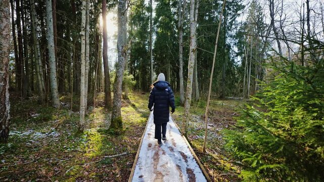 Static camera captures woman passing along snowy boardwalk in warm morning light