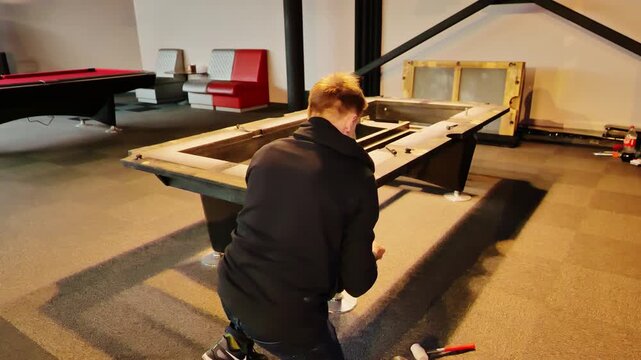 Focused repairman adjusts billiard hardware while restoring sturdy table frame.