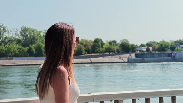 Thoughtful woman with sunglasses standing on a bridge, admiring the view of the Rhine River and the Breisach agricultural dam in summer
