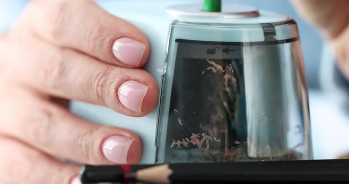In a cozy workspace, hands skillfully operate a pencil sharpener. Colorful shavings dance and swirl, transforming into a mini art display that captures creativity.