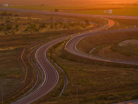 Aerial view of the winding A0 ring road highway interchange near Bucuresti bathed in warm golden sunrise light, showcasing modern transport infrastructure.