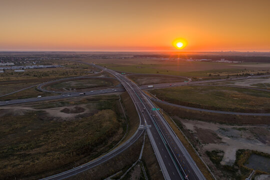 Aerial sunrise view over the modern A0 ring motorway junction near Bucuresti, showcasing highway infrastructure, light traffic and scenic golden morning horizon.