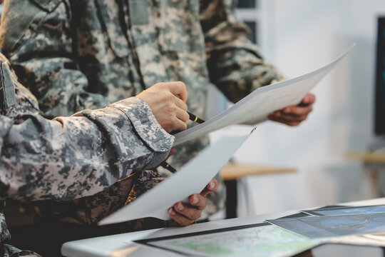 Close-up of military personnel in camouflage uniforms reviewing documents and maps at a table during a planning meeting.