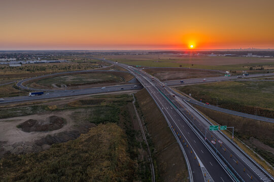Aerial view of the modern A0 ring motorway intersection near Bucuresti at vibrant golden sunrise, showcasing transport infrastructure and light traffic concept.