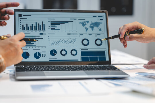 Business team reviews financial charts and analytics dashboard on a laptop during a planning meeting at an office desk.