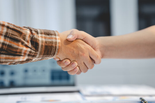 Close-up of two people shaking hands across a desk in a bright office, showing agreement, trust, partnership and successful business communication.