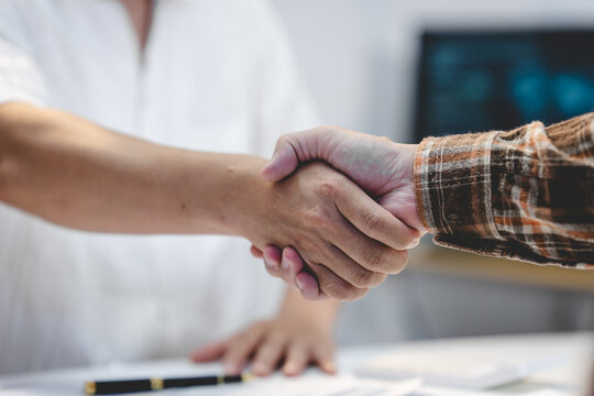 Close-up of two people shaking hands across a desk in a bright office, showing agreement, trust, partnership and successful business cooperation.