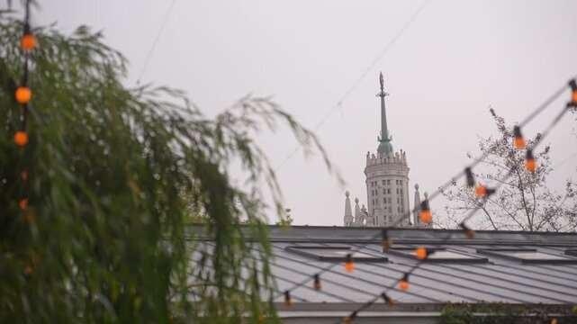 Ornate historic tower with green spire framed by rooftop foliage and diagonal string lights, with tower, spire, statue, architecture detail, showing historic, building, facade, stone context