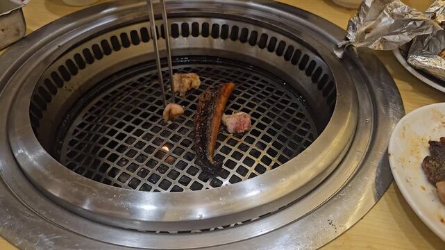 man washing machine,Grilled meat and eel sizzles over a hot, circular grill. Tongs flip pieces as flames rise beneath the grate. Fingers hover, ready to adjust the cooking. 