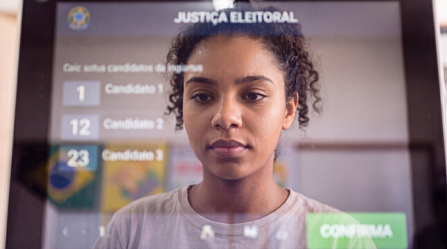 Young Brazilian woman looking at electronic voting machine screen with candidate list. Female voter at polling station in Brazil