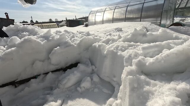A Winter Scene Featuring Freshly Fallen Snow Accumulated on Surfaces Amidst a Bright Sunlit Sky and Glimmering Greenhouse Structures
