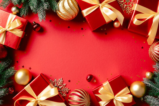 Christmas gifts, fir branches, and golden baubles frame on red background
