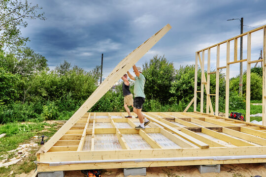 Wall raising by two builders manually lifting completed wall frame into vertical position during construction of timber frame house.