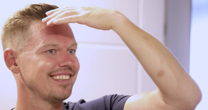 In a bright and stylish salon, a man enjoys his grooming time, smiling and checking his hairstyle in the mirror. His joy is contagious as he admires the fresh look.