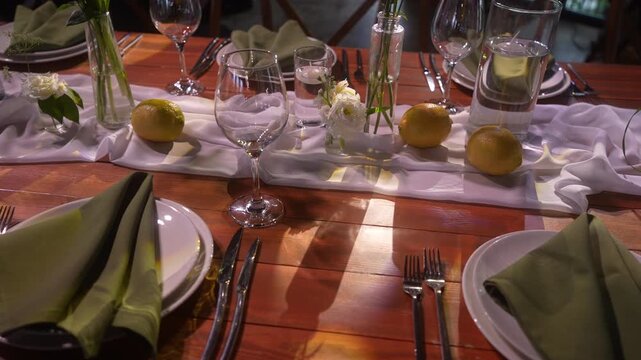 Rustic-chic table setting with shifting glass reflections over white runner and lemons, with table, runner, glass, vase detail, showing flower, lemon, napkin, plate context