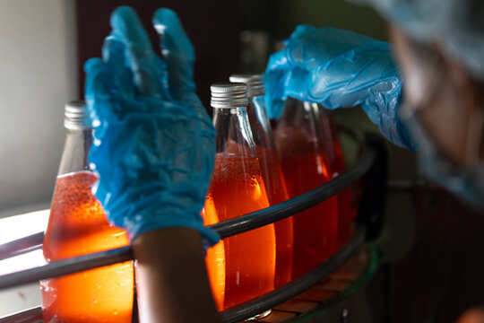 Close up of hand of factory worker holding bottle of orange juice.