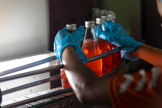 Close up of hand of factory worker holding bottle of orange juice.