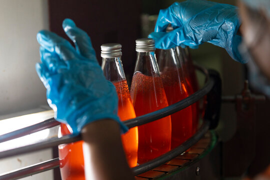 Close up of hand of factory worker holding bottle of orange juice.