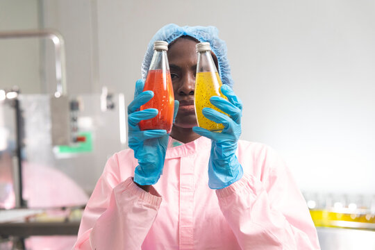 Black woman inspecting drink quality with rows of glass bottles on the automated conveyor system in manufacturing assembly line.