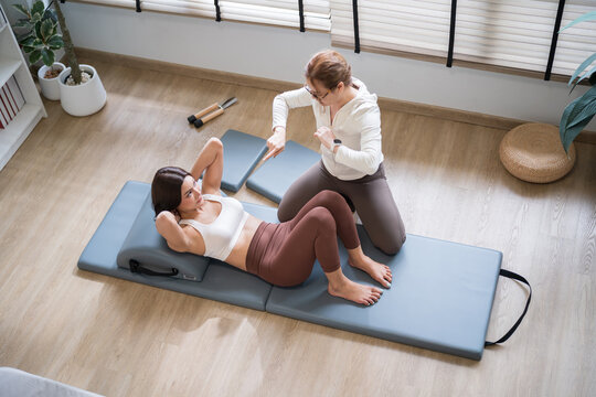 Asian Pilates Instructor Assisting Pilates Abdominal Curl on Spine Corrector