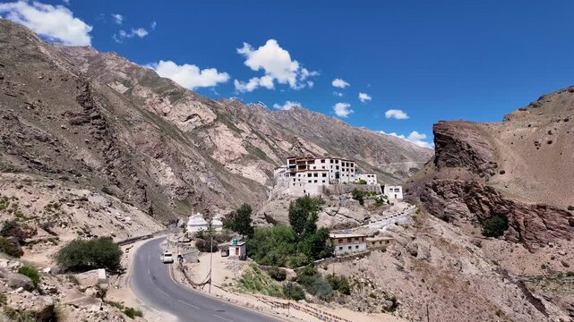 Padum, India : High angle tilt down footage of of mountain road by Bardan Gompa, Buddhist monastery on rocky outcrop in near Padum of Zanskar valley in Ladakh, India on sunny day