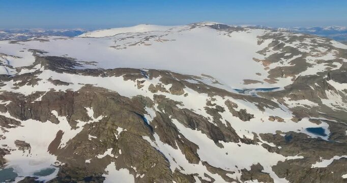 4K video; Slow backward drone flight over fjell (mountain plateau) in southern Norway with half frozen lakes, bare rocks and patches of melting snow in spring. 