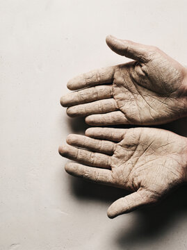 Hands covered in dry clay against neutral plaster wall, cracked textured skin, artisan pottery aesthetic in warm earthy monochrome tones