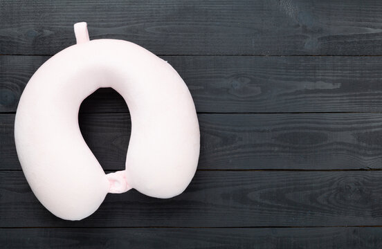 Pink travel pillow on wooden background, top view