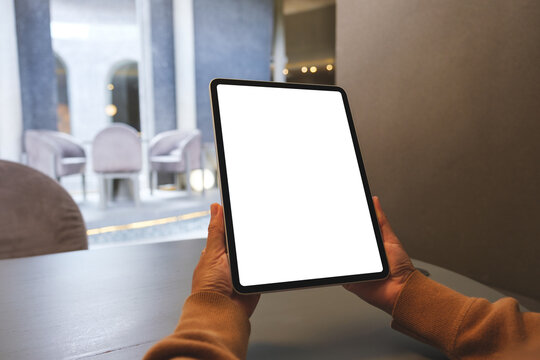 Mockup image of a woman holding digital tablet with blank white desktop screen in cafe