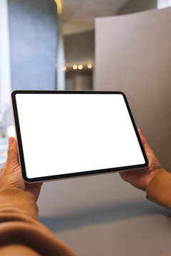 Vertical mockup image of a woman holding digital tablet with blank white desktop screen in cafe