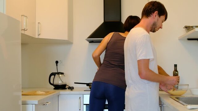 Young couple prepares homemade lunch together in bright cozy kitchen. They cut vegetables, stir food, laugh, and enjoy simple joy of cooking side by side. Shared chores turn into connection and care.