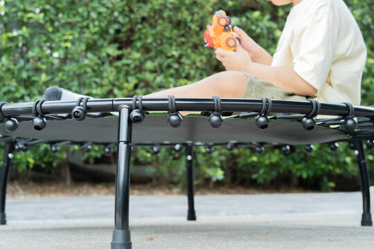A little boy sitting cross-legged on a blck mini trampoline while playing his car toy
