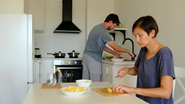 Young couple prepares homemade lunch together in bright cozy kitchen. They cut vegetables, stir food, laugh, enjoy simple joy of cooking side by side. Shared chores turn into connection and care.