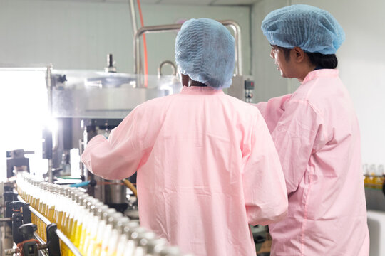 Two factory workers monitoring cold drink bottles on production line at drinks production plant.