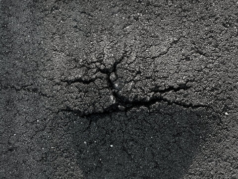 Close up top down view of dark cracked asphalt texture showing road damage and urban decay