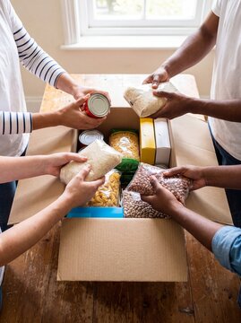 Food drive volunteers packing box cans rice pasta donation charity a diverse group fills a cardboard box with canned goods rice pasta for food drive promotion and community nutrition campaigns