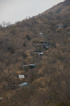 Vertical view from the ground looking up at the steep mountain slope and pilgrimage trail with local shops among dry forest trees under an overcast cloudy sky at Khao Wong Phrachan in Lopburi Thailand