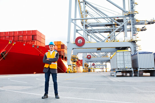 Man, freight and portrait on dock with arms crossed, service or international courier with helmet. Male person, confidence and professional pride at logistics port, shipping industry and export