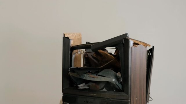 Close-up motion scene of person striking damaged wooden speaker cabinet with mallet, exposing torn particleboard, bent metal support, crushed speaker cones and rough repair damage under studio light
