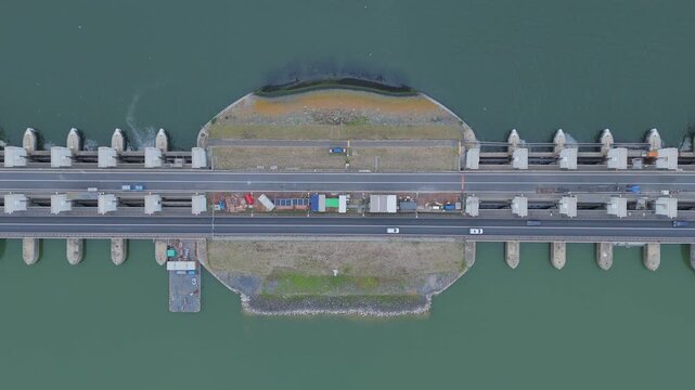 Top down aerial drone view of the Lorentz Locks on the Afsluitdijk in the Netherlands, showing cars driving along the road above the lock complex and surrounding water infrastructure.
