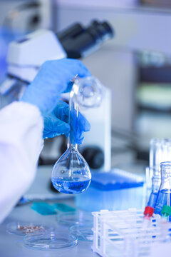 The gloved hands of a medical research scientist drawing the empty bottle back upward at a professional laboratory workstation, in a clean and modern laboratory.
