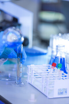 The gloved hands of a medical research scientist tipping the flask further to speed the pour inside a clean pharmaceutical research laboratory, in a clean and modern laboratory.