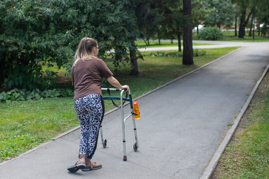 A young woman with cerebral palsy walks in a park with a walker.