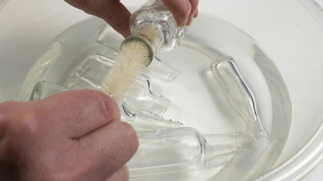 Human washing small glass bottle with bottle brush in a bowl with water, household chores