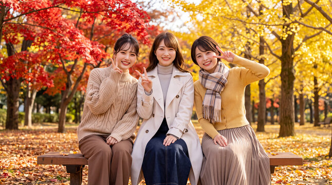 紅葉した公園のベンチで笑顔でピースサインをする女性3人（秋の行楽・女子旅・紅葉狩り）