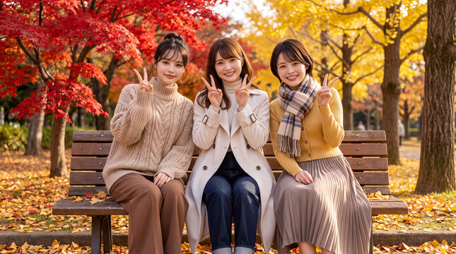 紅葉した公園のベンチで笑顔でピースサインをする女性3人（秋の行楽・女子旅・紅葉狩り）