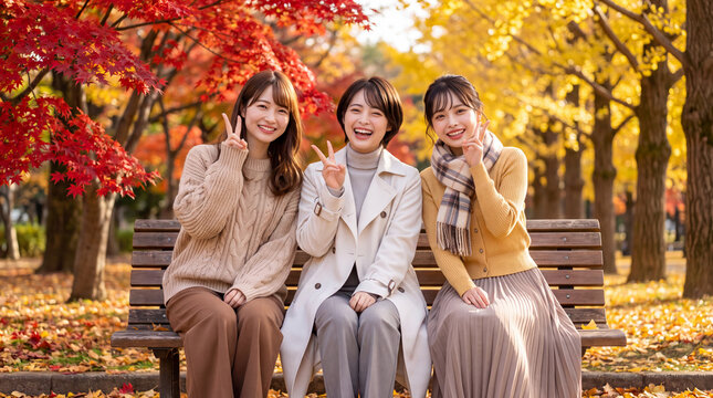 紅葉した公園のベンチで笑顔でピースサインをする女性3人（秋の行楽・女子旅・紅葉狩り）